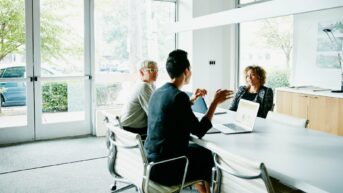 a group of people sitting around a table with laptops