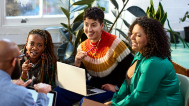 three people sitting on a couch with laptops