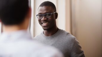 a man wearing glasses is smiling at another man