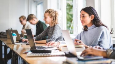 a group of people sitting at a table with laptops
