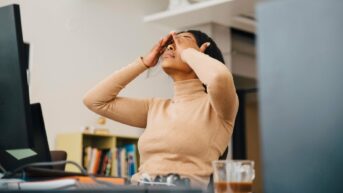 a woman sitting at a desk with her hands on her head