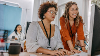 two women sitting at a table with a laptop
