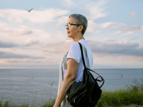 a woman with a black bag walking on a path near the ocean