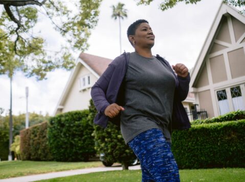 a woman in a gray shirt and blue leggings running in front of a