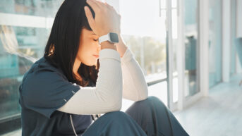 a healthcare worker sitting on the floor with her head in her hands