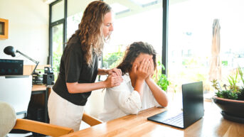 a woman is covering her face with her hands in front of a laptop