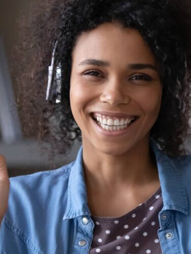 a woman smiling and waving her hand in front of a bookshelf