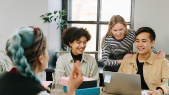 a group of people sitting around a table with laptops