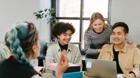 a group of people sitting around a table with laptops