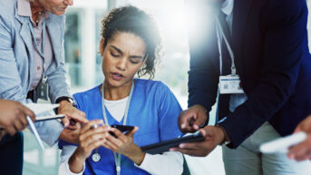 Frustrated female healthcare worker showing signs of burnout while multitasking with team